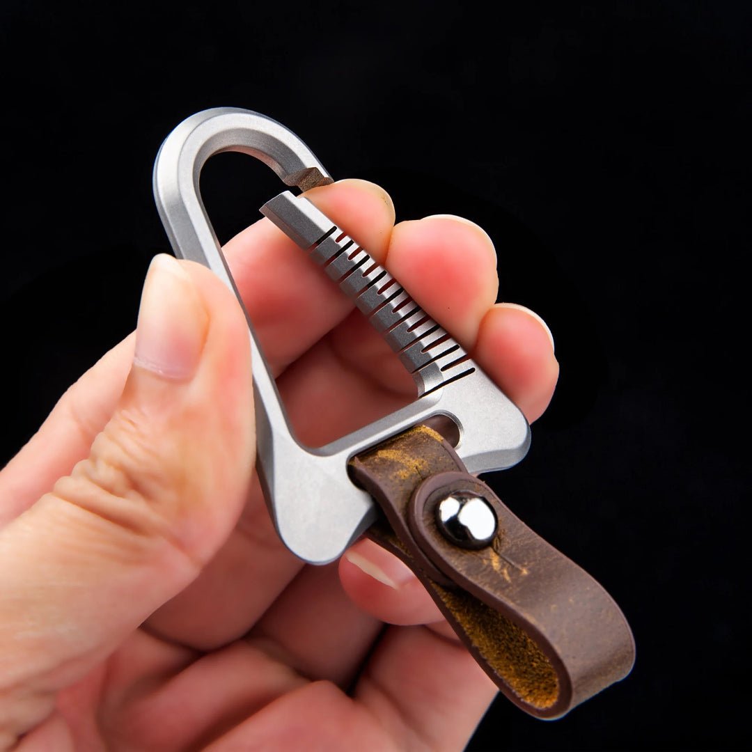 Hand holding a keychain with a carabiner and leather strap against a black background