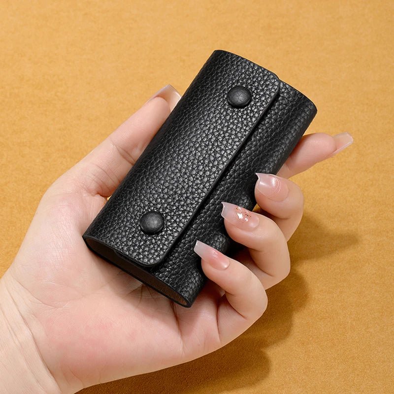 Hand holding a black textured wallet against a beige background