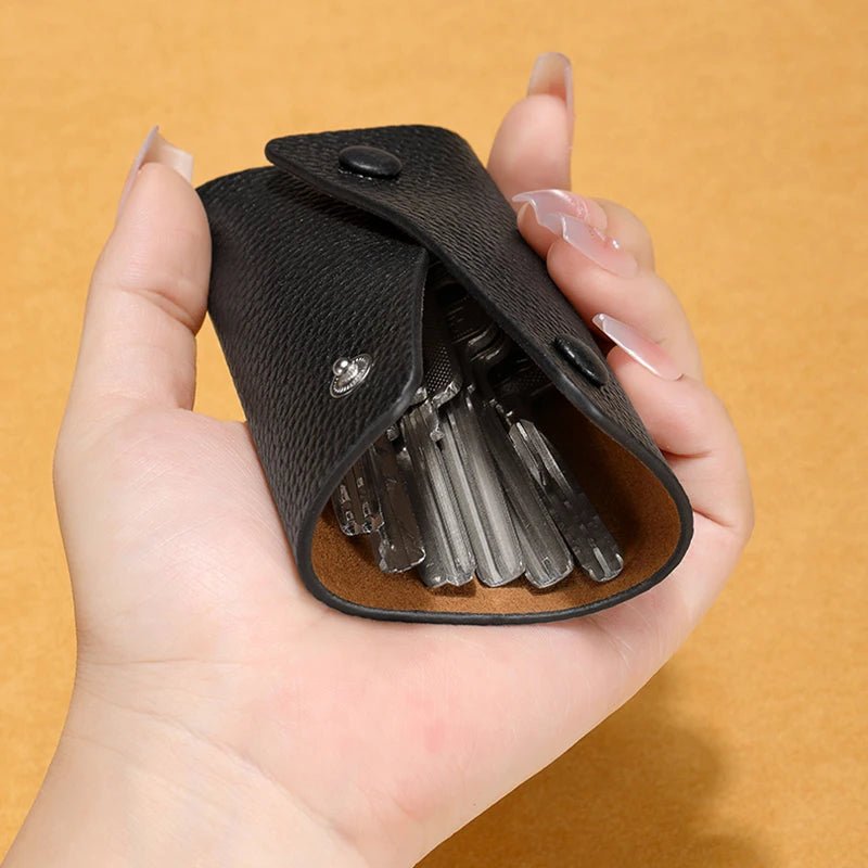 Hand holding a black key organizer with keys against an orange background