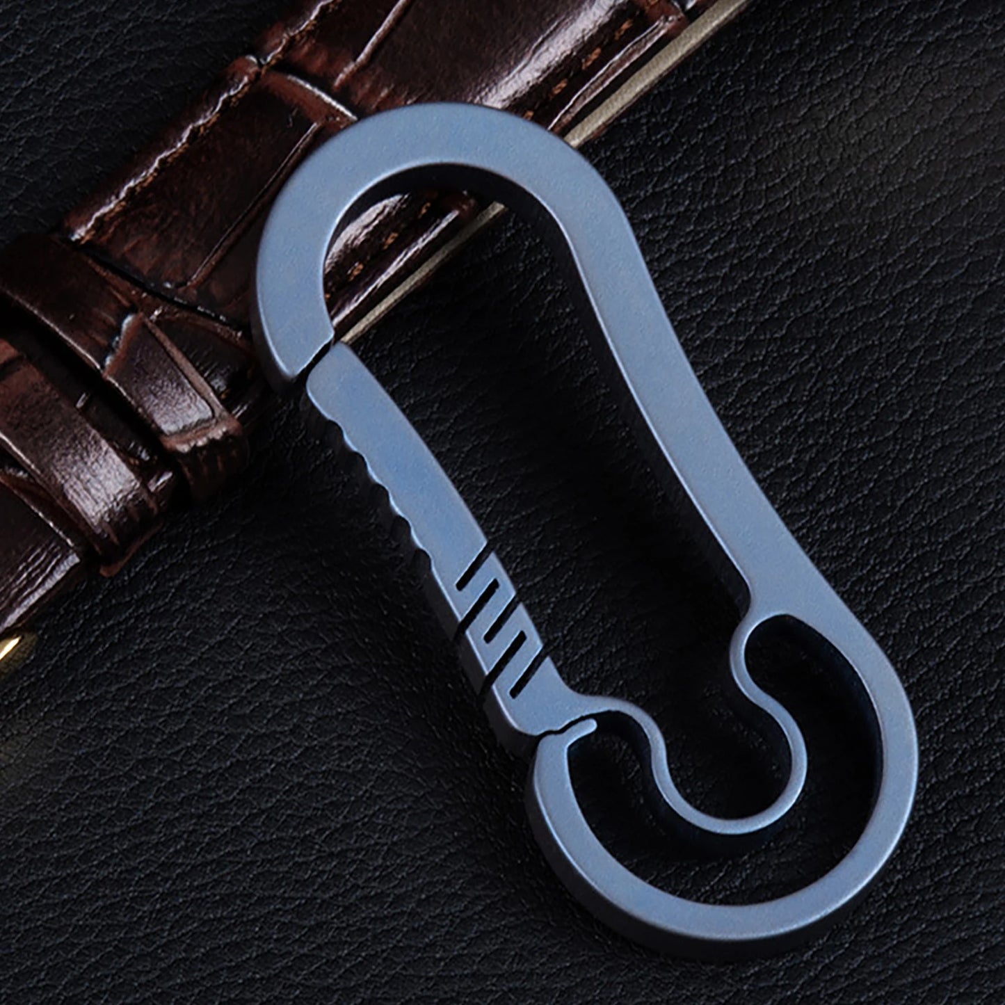 Blue carabiner leaning on a leather strap on a dark background.