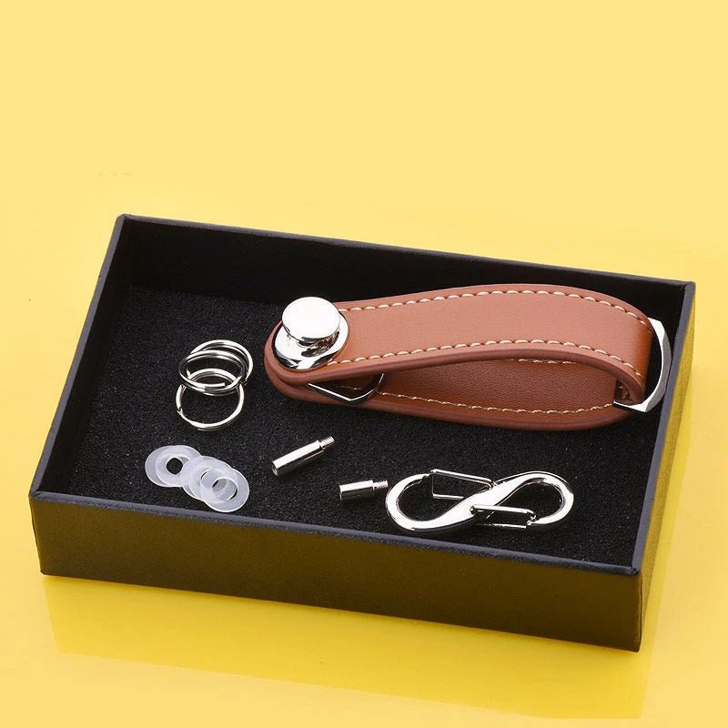 Set of metal components and a brown leather key organizer in a black box on a yellow background.