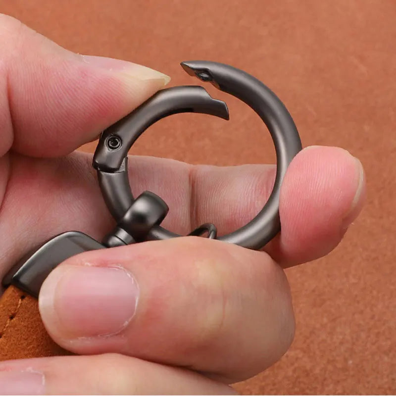 Metal carabiner held in a hand against a brown leather background