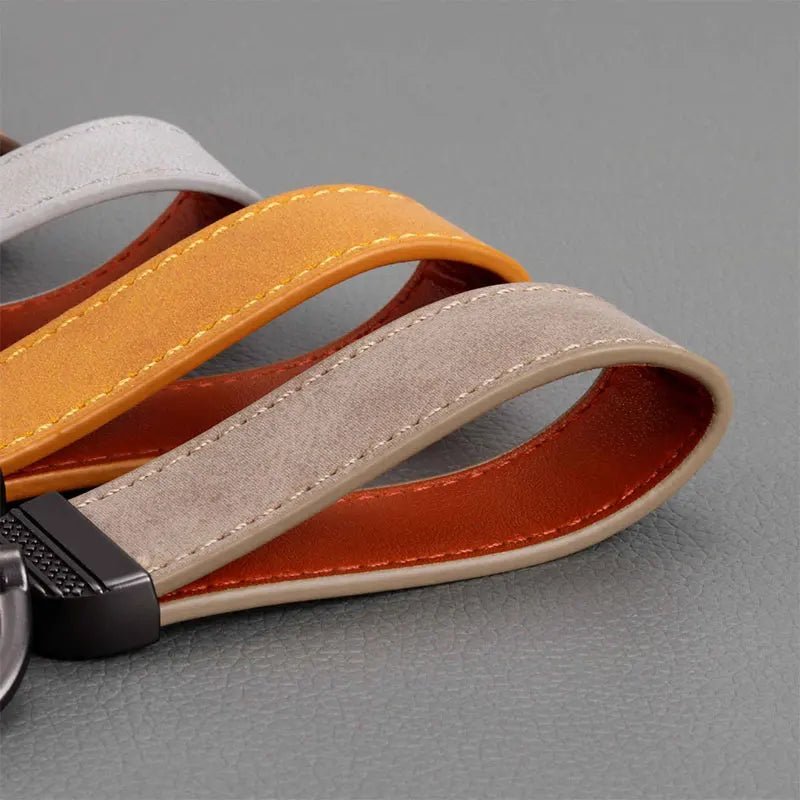 Close-up of a keychain with orange, gray, and brown leather straps on a gray background