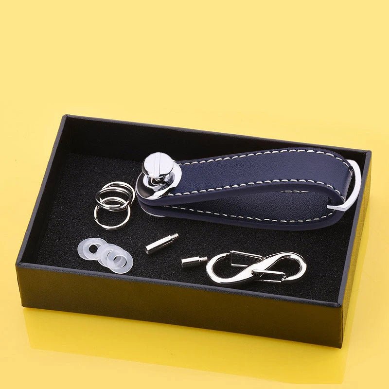 Set of metal compontents and navy blue leather key organizer in a black box on a yellow background.