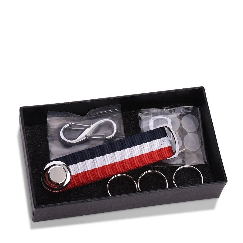 Set of metal components and blue, white and red striped nylon key organizer in black box on white background.