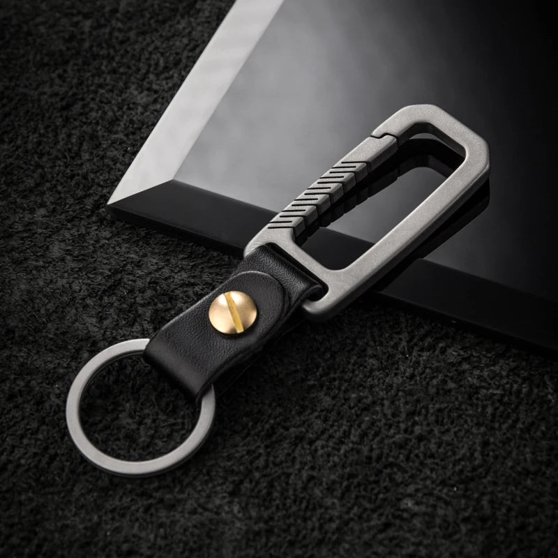 Titanium carabiner with leather strap and metallic clip on a dark textured background.