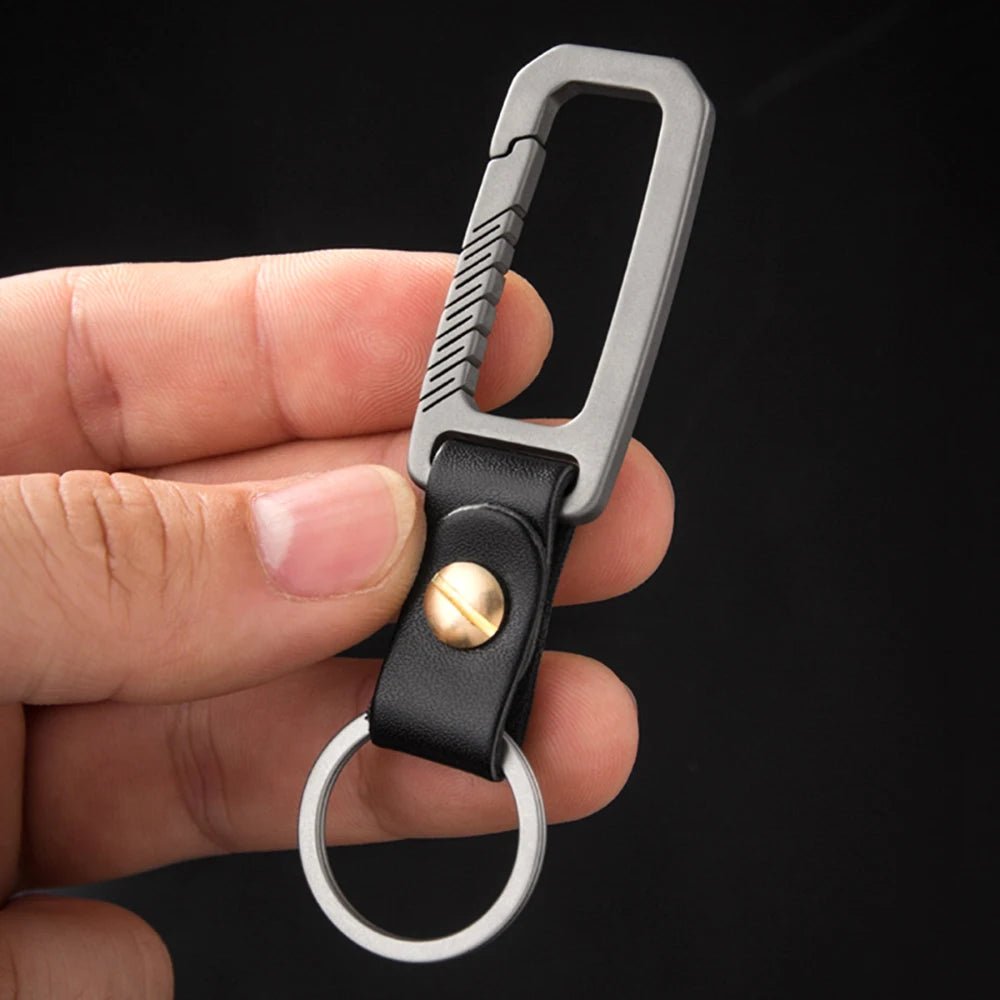 Keychain with black leather strap and gold accent held in a hand against a black background.