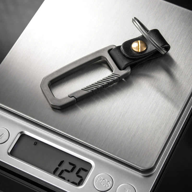 Titanium carabiner with a black leather strap and gold detail on a digital kitchen scale displaying weight.