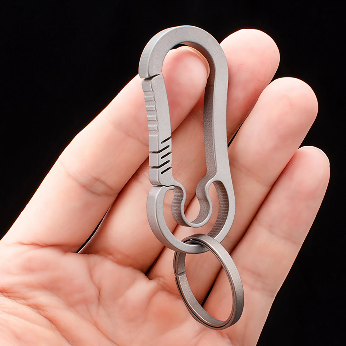 Metallic carabiner held in a hand against a black background.