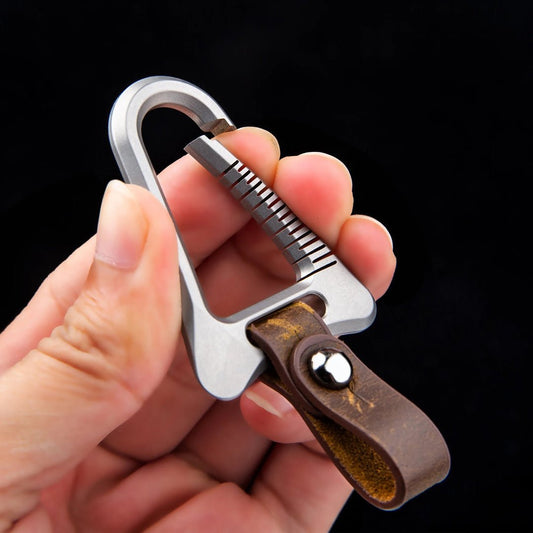 Hand holding a keychain with a carabiner and leather strap against a black background