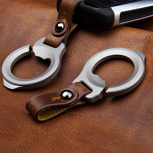 Two silver titanium keychains with brown leather straps on a brown leather surface.