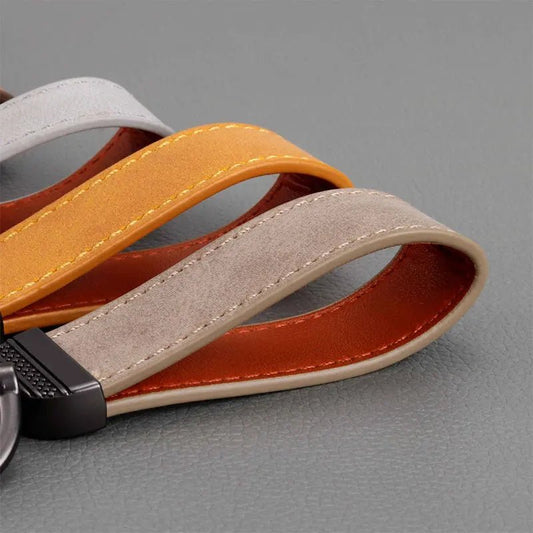 Close-up of a keychain with orange, gray, and brown leather straps on a gray background