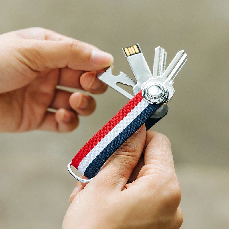Multitool keychain with USB drive and keys held by a hand against a neutral background.
