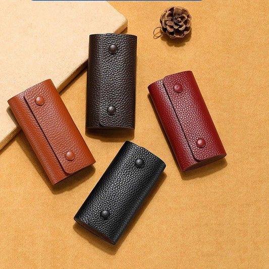 Four leather key cases in brown, black, and red on a beige surface.